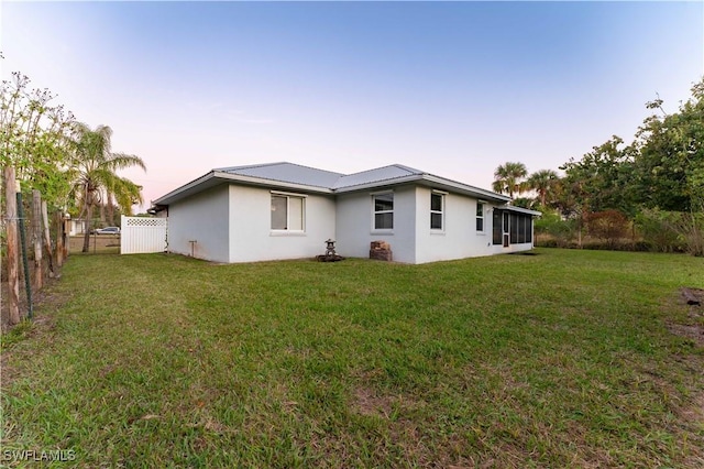 back of property at dusk featuring a fenced backyard, metal roof, a lawn, and stucco siding