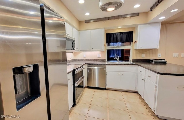 kitchen featuring dark countertops, appliances with stainless steel finishes, white cabinetry, a sink, and a peninsula