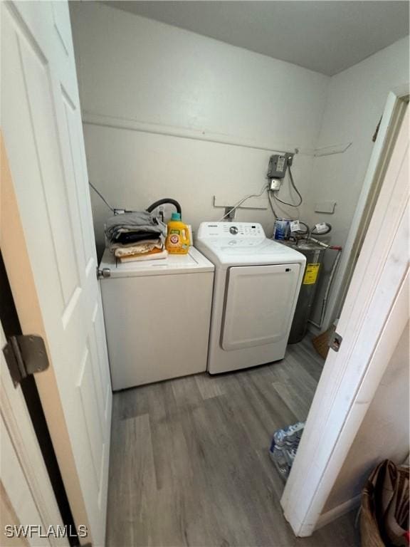 clothes washing area with washing machine and dryer, wood-type flooring, and electric water heater