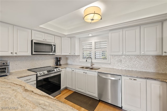 kitchen featuring sink, white cabinetry, light wood-type flooring, appliances with stainless steel finishes, and a tray ceiling