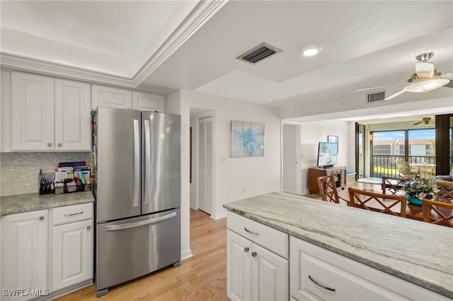 kitchen featuring tasteful backsplash, light wood-type flooring, stainless steel fridge, light stone countertops, and white cabinets