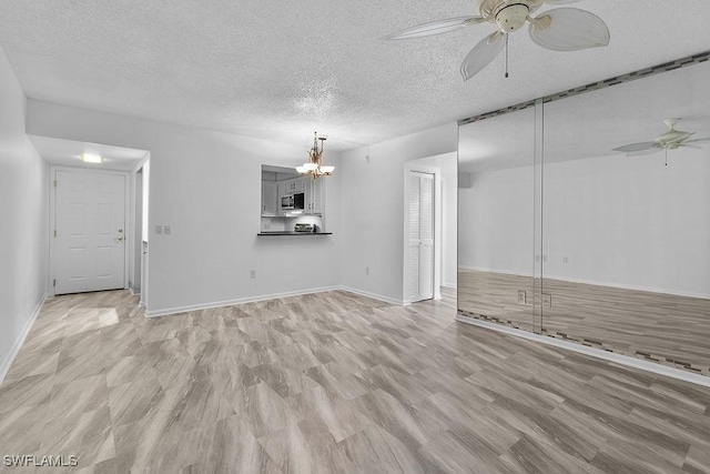 unfurnished living room featuring ceiling fan with notable chandelier, light hardwood / wood-style flooring, and a textured ceiling