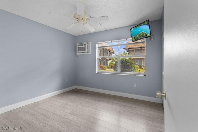 empty room with a textured ceiling, a wall unit AC, light hardwood / wood-style floors, and ceiling fan