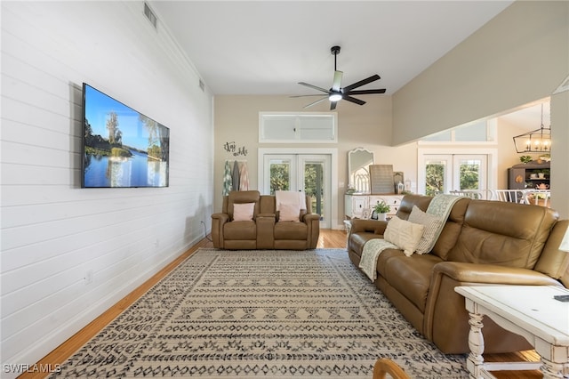 living room with ceiling fan with notable chandelier, light hardwood / wood-style flooring, french doors, and a towering ceiling