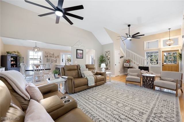 living room with ceiling fan with notable chandelier, light hardwood / wood-style flooring, and high vaulted ceiling