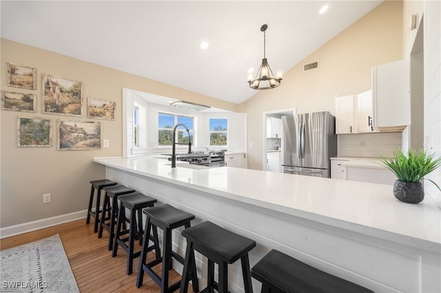 kitchen with sink, white cabinetry, hanging light fixtures, stainless steel fridge, and kitchen peninsula