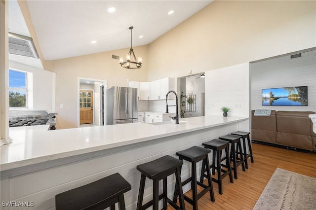 kitchen featuring a kitchen bar, hanging light fixtures, light wood-type flooring, stainless steel fridge, and kitchen peninsula