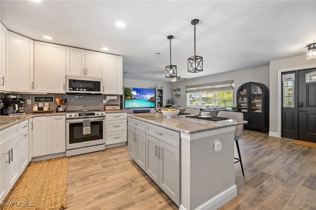 kitchen with a kitchen island, appliances with stainless steel finishes, pendant lighting, white cabinets, and light stone counters