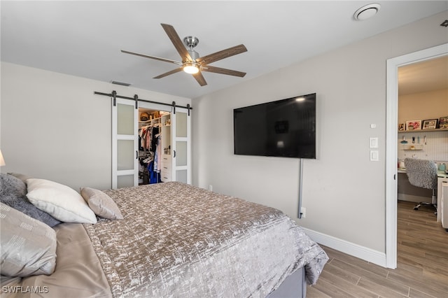 bedroom with a walk in closet, ceiling fan, light hardwood / wood-style floors, a barn door, and a closet