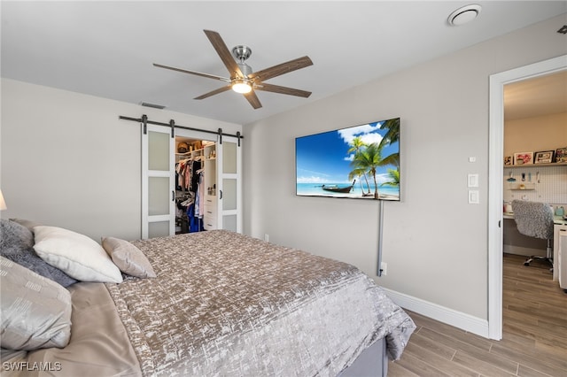 bedroom with a spacious closet, a closet, ceiling fan, a barn door, and light hardwood / wood-style floors