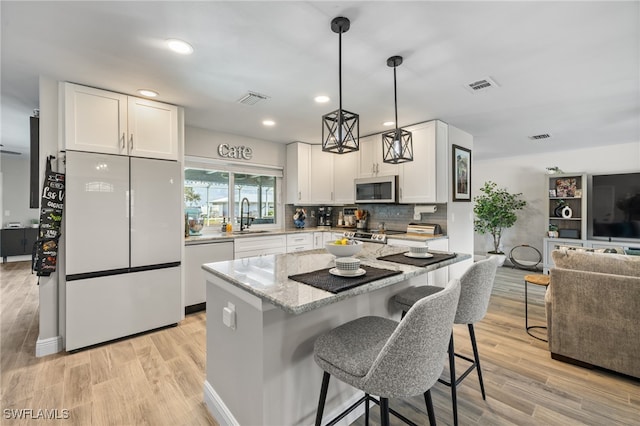 kitchen featuring white cabinetry, hanging light fixtures, light stone counters, light hardwood / wood-style floors, and stainless steel appliances