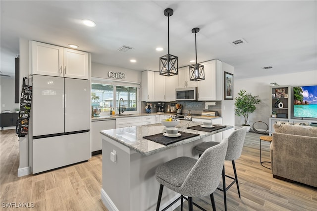 kitchen with light hardwood / wood-style flooring, stainless steel appliances, a kitchen breakfast bar, light stone countertops, and white cabinets