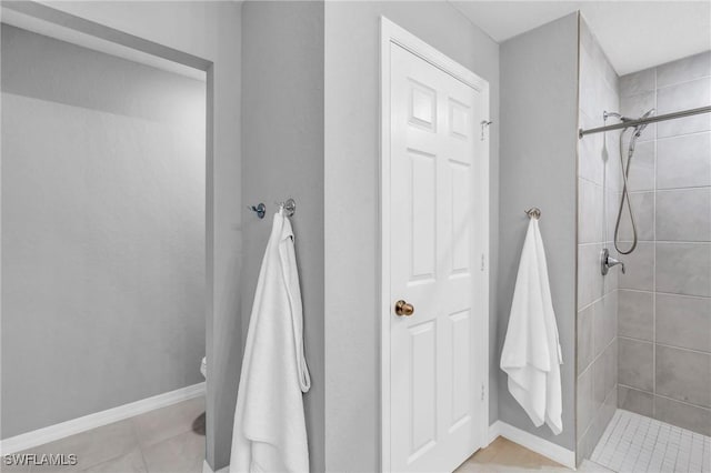 bathroom with toilet, tile patterned flooring, and a tile shower