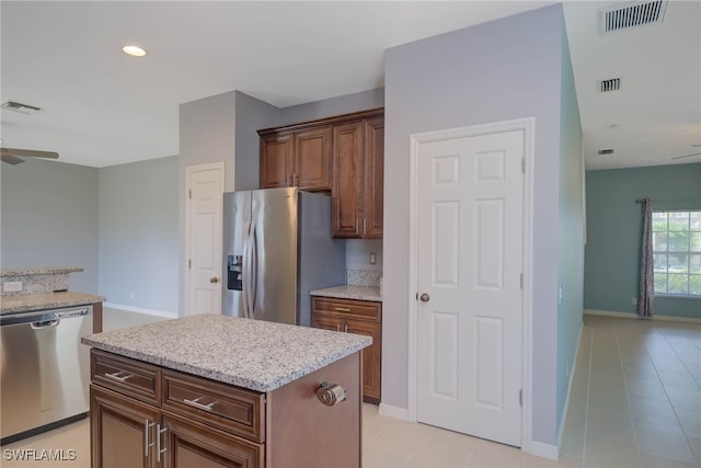 kitchen with light tile patterned flooring, light stone counters, appliances with stainless steel finishes, a kitchen island, and ceiling fan