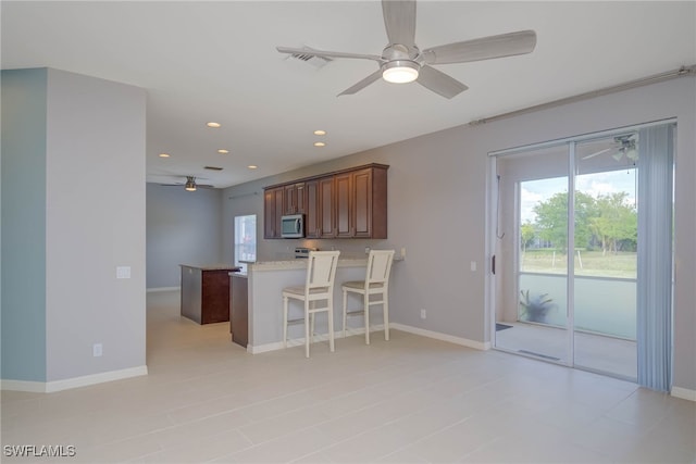 kitchen with ceiling fan, a kitchen bar, a kitchen island, and plenty of natural light