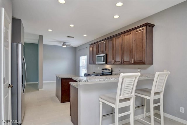 kitchen with a breakfast bar, kitchen peninsula, ceiling fan, light stone counters, and stainless steel appliances