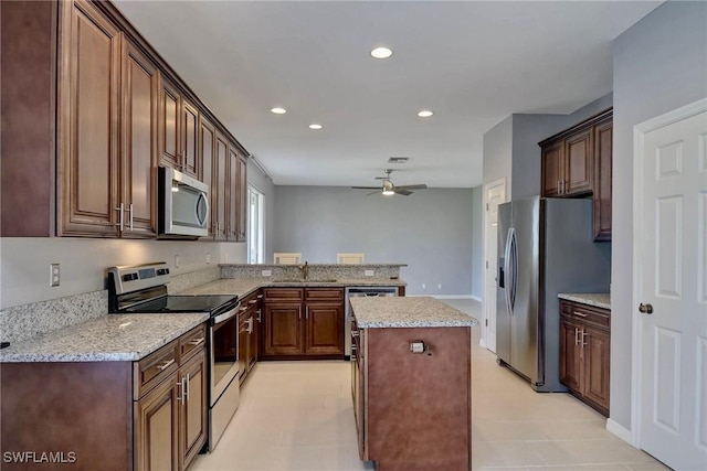 kitchen featuring a kitchen island, appliances with stainless steel finishes, sink, ceiling fan, and light stone counters