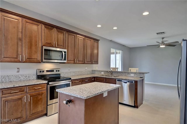 kitchen featuring sink, light stone counters, kitchen peninsula, a kitchen island, and stainless steel appliances