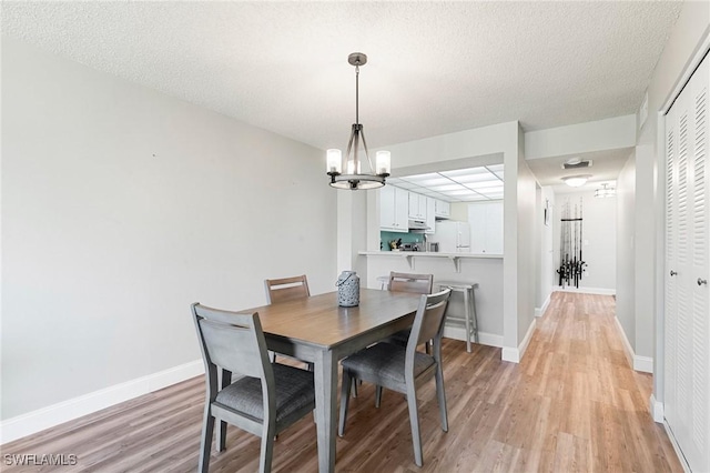 dining area featuring a textured ceiling, a notable chandelier, and light wood-type flooring