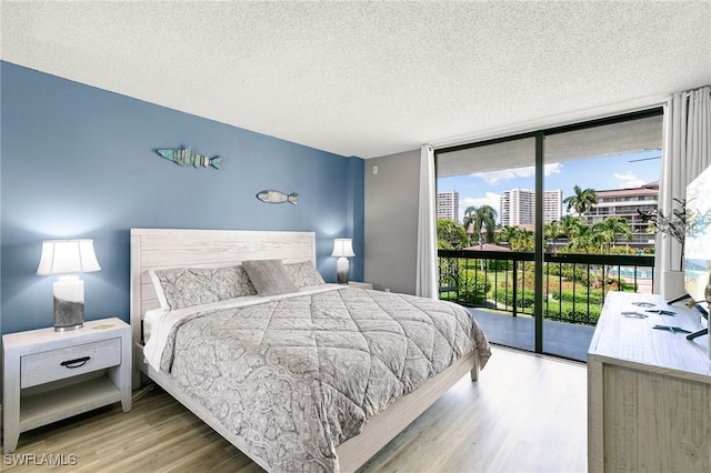 bedroom featuring expansive windows, access to exterior, light hardwood / wood-style flooring, and a textured ceiling