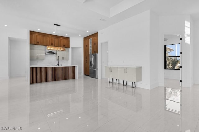 kitchen with sink, hanging light fixtures, stainless steel fridge, kitchen peninsula, and range hood