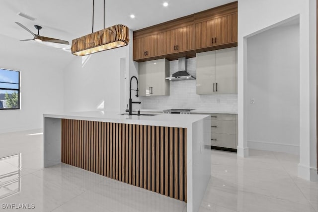 kitchen featuring sink, decorative light fixtures, an island with sink, wall chimney range hood, and backsplash