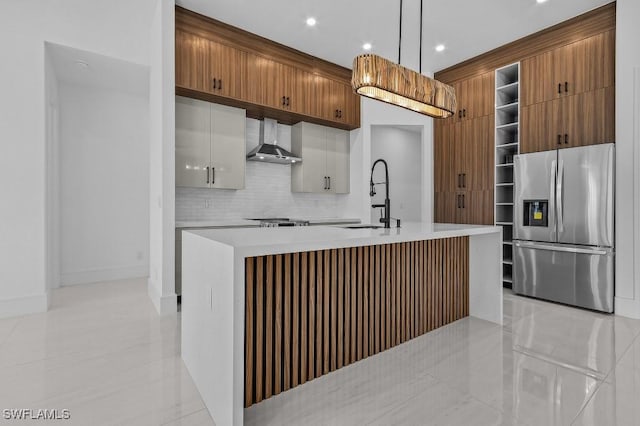 kitchen featuring sink, decorative light fixtures, stainless steel fridge with ice dispenser, an island with sink, and wall chimney range hood