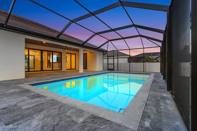 pool at dusk featuring glass enclosure and a patio area