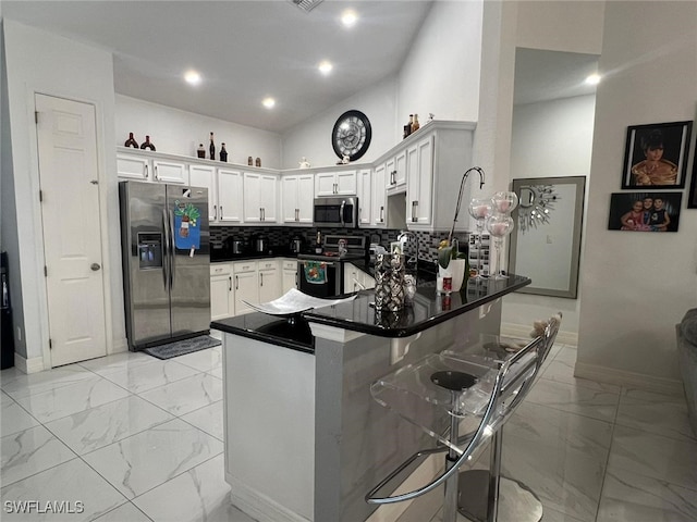 kitchen with a kitchen bar, white cabinetry, tasteful backsplash, appliances with stainless steel finishes, and kitchen peninsula