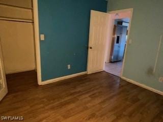 unfurnished bedroom featuring fridge, dark hardwood / wood-style flooring, and a closet