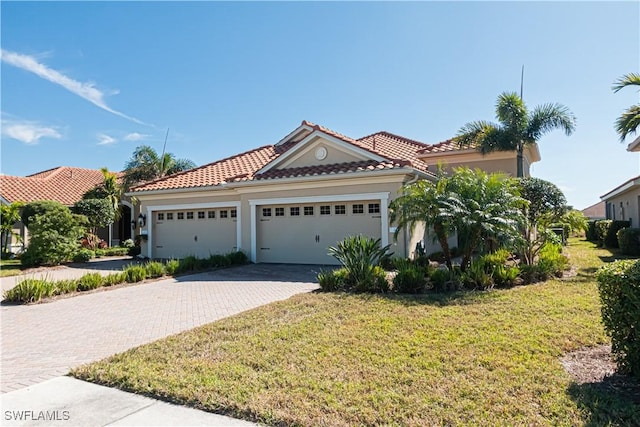 mediterranean / spanish-style house with decorative driveway, a front yard, an attached garage, and a tile roof