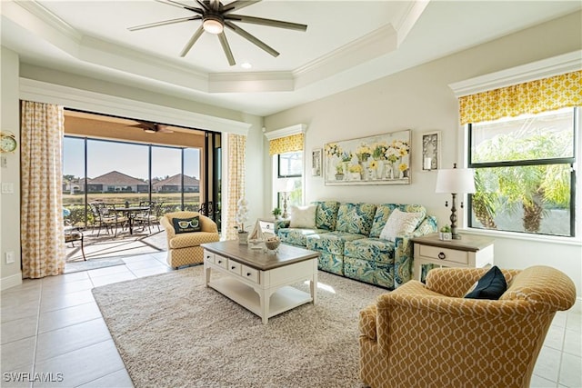 living room featuring ceiling fan, ornamental molding, a tray ceiling, and light tile patterned floors