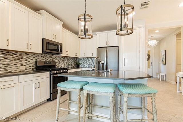 kitchen with appliances with stainless steel finishes, pendant lighting, white cabinetry, light tile patterned floors, and a center island with sink