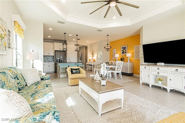 living room featuring ceiling fan, ornamental molding, a tray ceiling, and light tile patterned floors