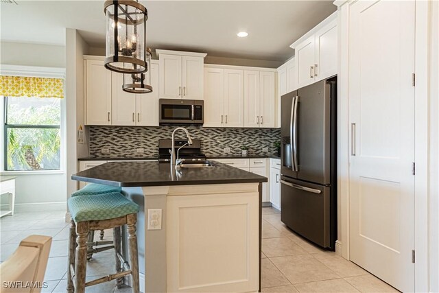 kitchen with appliances with stainless steel finishes, an island with sink, sink, hanging light fixtures, and light tile patterned floors