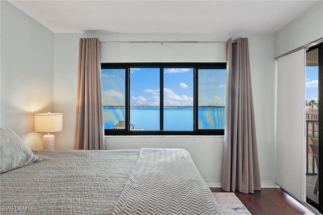 bedroom with dark wood-style flooring and a water view