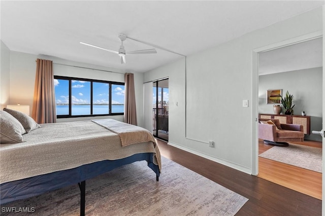 bedroom featuring access to exterior, a water view, ceiling fan, wood finished floors, and baseboards