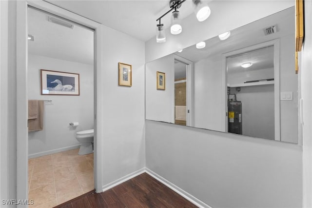 bathroom featuring toilet, wood finished floors, visible vents, baseboards, and water heater