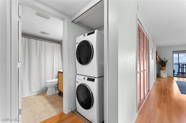 laundry room featuring light wood-type flooring, stacked washer / dryer, laundry area, and visible vents