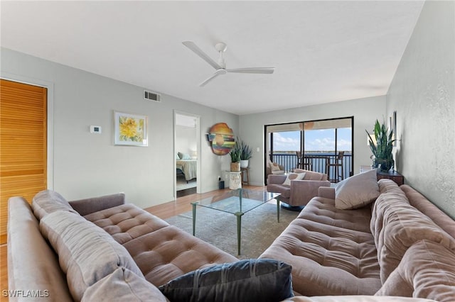 living area with a ceiling fan, visible vents, a textured wall, and wood finished floors