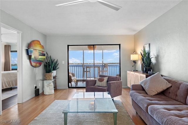 living room with light wood-type flooring, a water view, ceiling fan, and baseboards