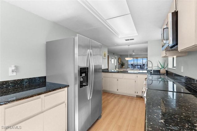 kitchen with a peninsula, light wood-style floors, appliances with stainless steel finishes, dark stone counters, and decorative light fixtures