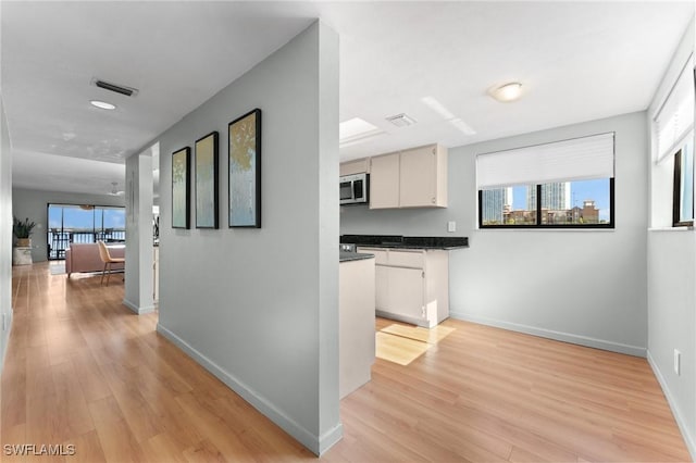 hallway with light wood-style flooring, visible vents, and baseboards