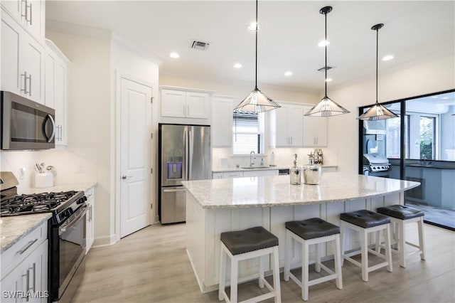 kitchen featuring hanging light fixtures, stainless steel appliances, white cabinets, and a kitchen island