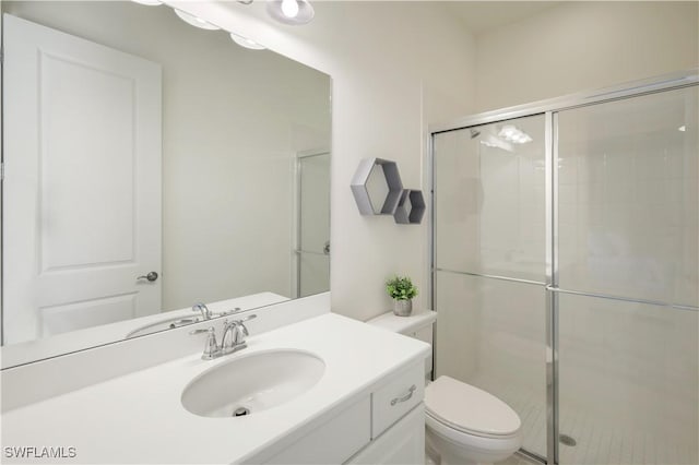 bathroom featuring toilet, vanity, and a shower with shower door