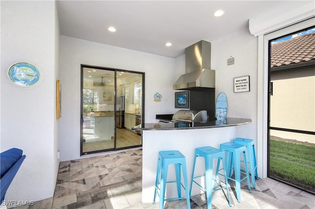 kitchen with a breakfast bar area, fridge, kitchen peninsula, exhaust hood, and dark stone counters