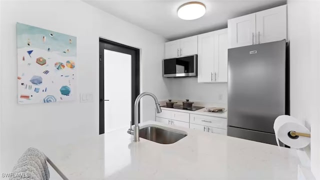 kitchen with light countertops, appliances with stainless steel finishes, a sink, and white cabinets