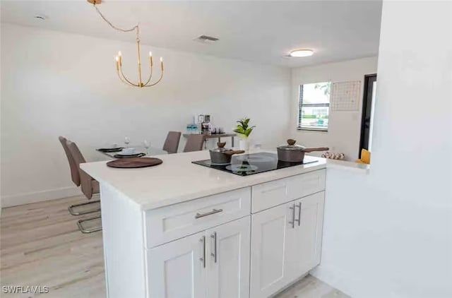 kitchen with light wood finished floors, light countertops, an inviting chandelier, white cabinetry, and black electric cooktop