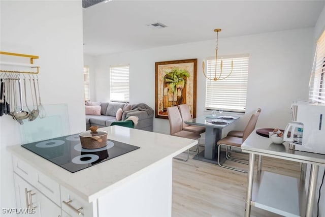 kitchen featuring black electric stovetop, visible vents, hanging light fixtures, light wood-style flooring, and white cabinets