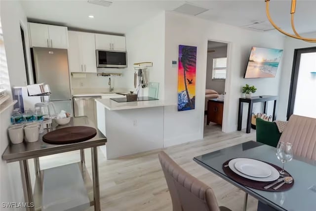 kitchen with appliances with stainless steel finishes, light countertops, light wood-type flooring, white cabinetry, and a sink